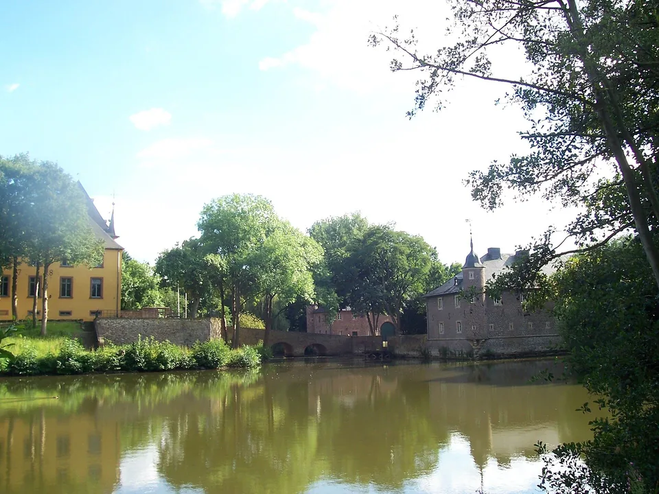 Schloss Burgau in Düren hinter einem von Bäumen gesäumten Weiher