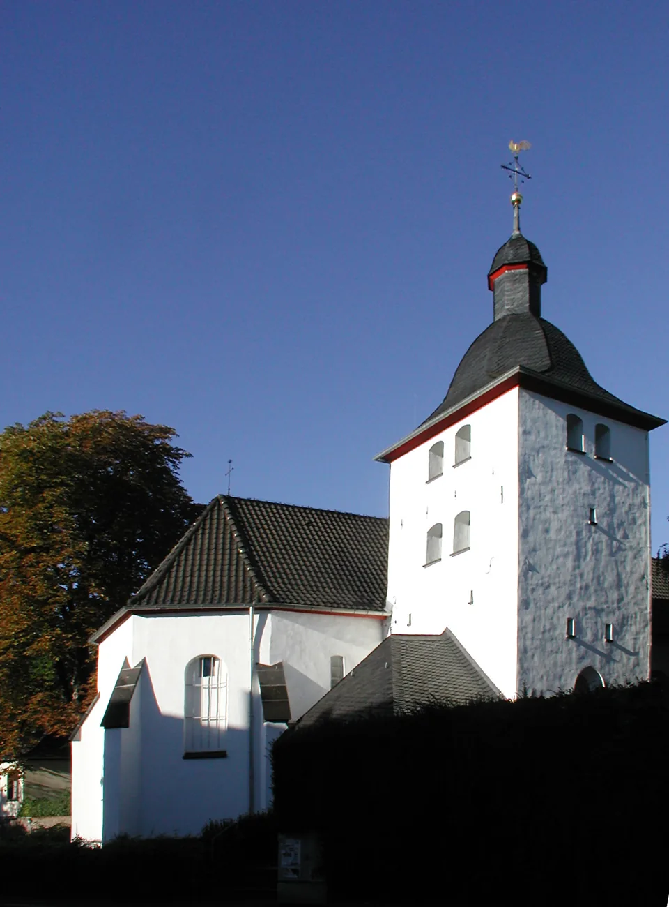 Weißer Kirchturm in Alt-Hürth vor blauem Himmel